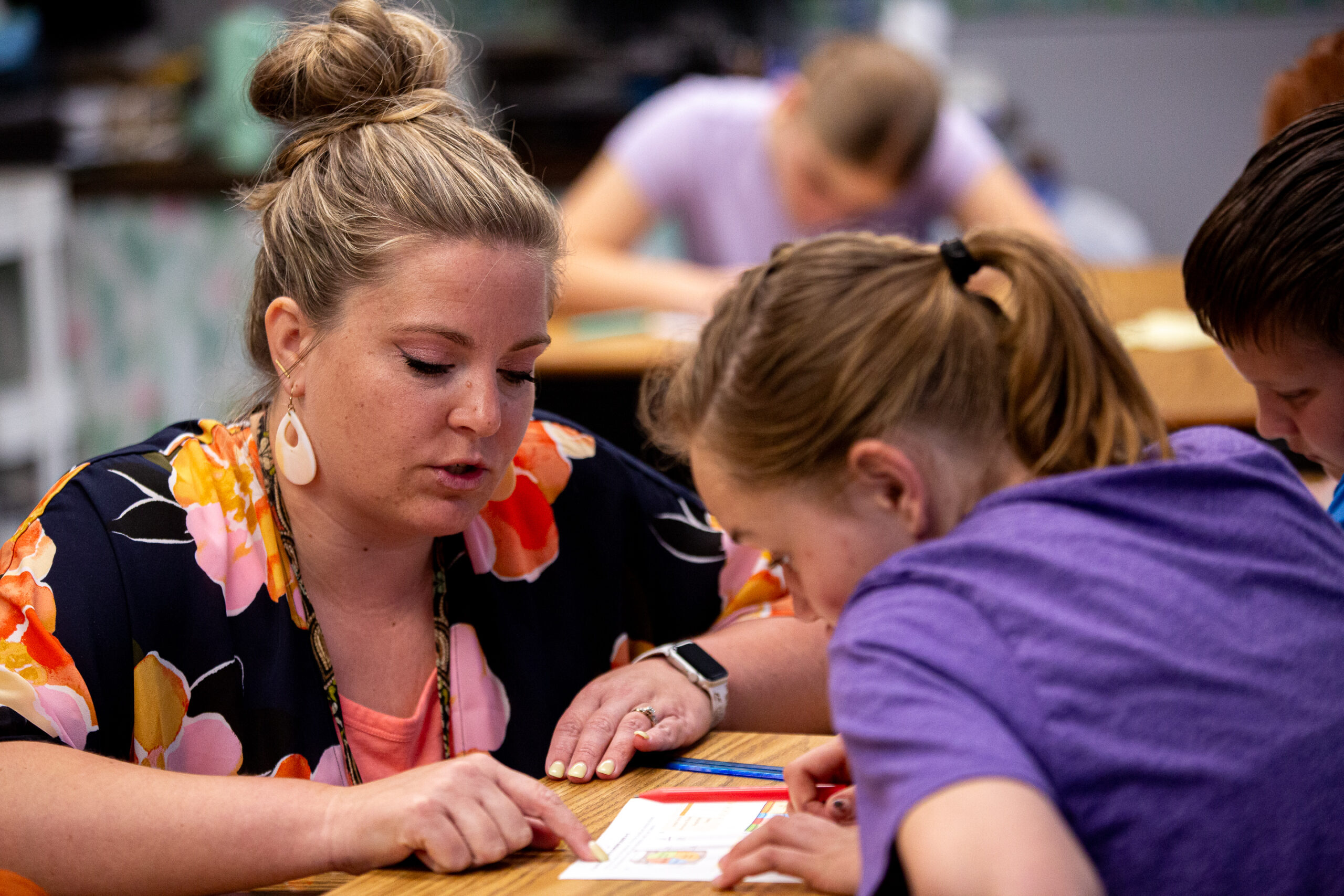 Teacher helps student with worksheet at classroom table